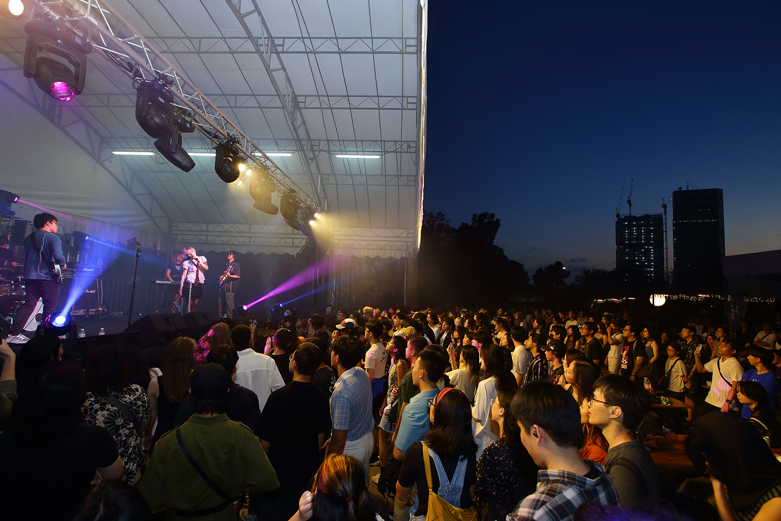 Image of music performance against a dark evening sky, with audiences standing in the mosh pit