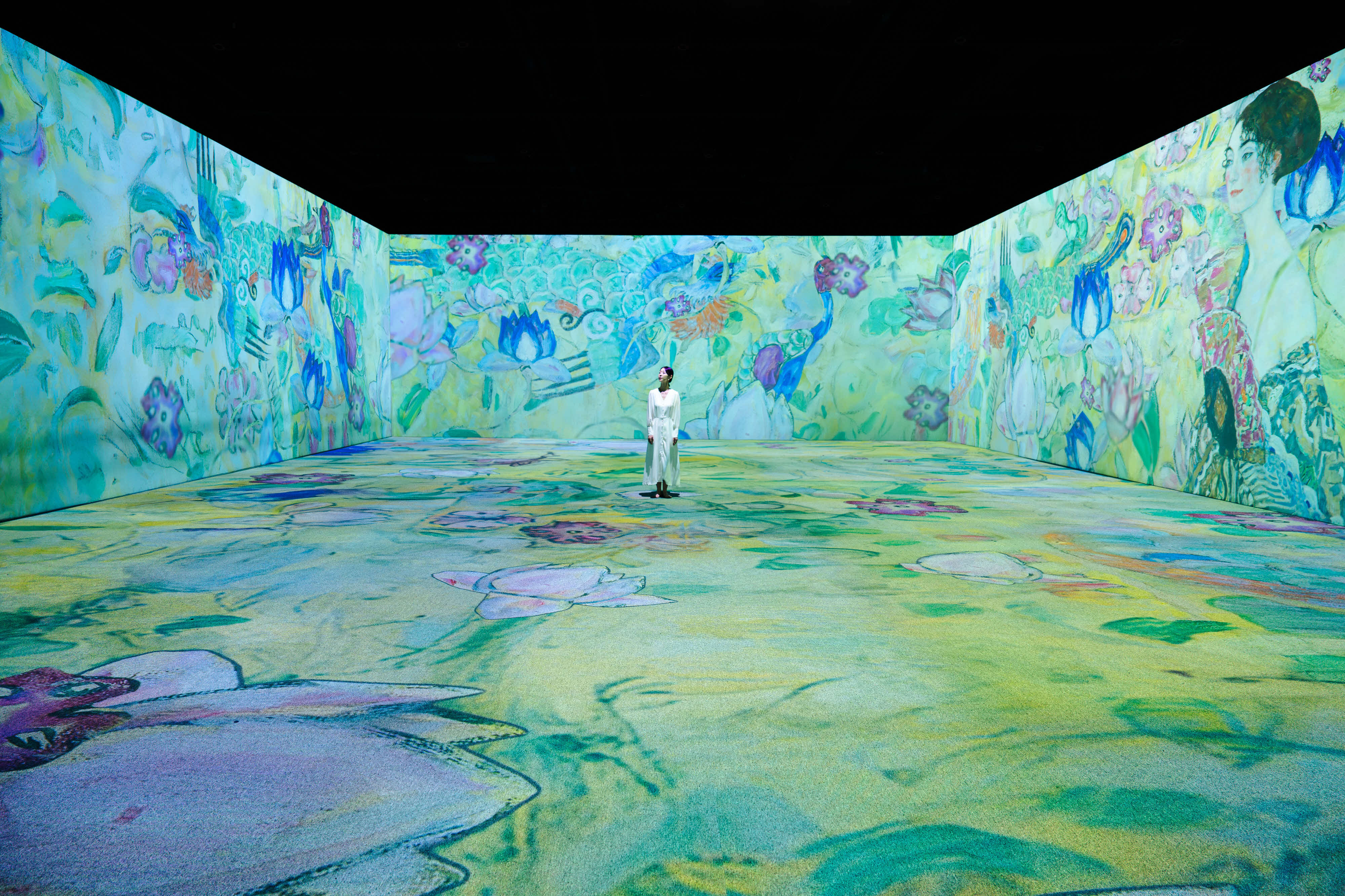 Image of a room surrounded in blue and green artwork projection by Gustav Klimt