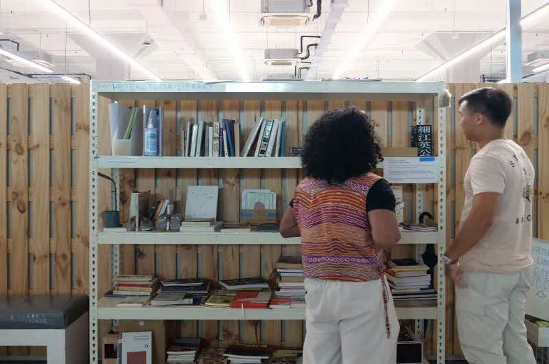 Image of two people with their backs facing the camera, looking at a shelf with books and writings