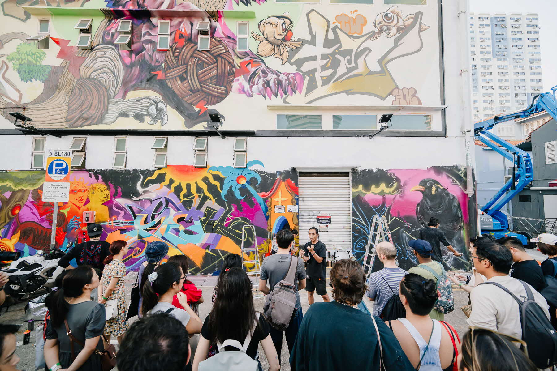 Image of a public graffiti mural wall and a tour guide speaking to an audience