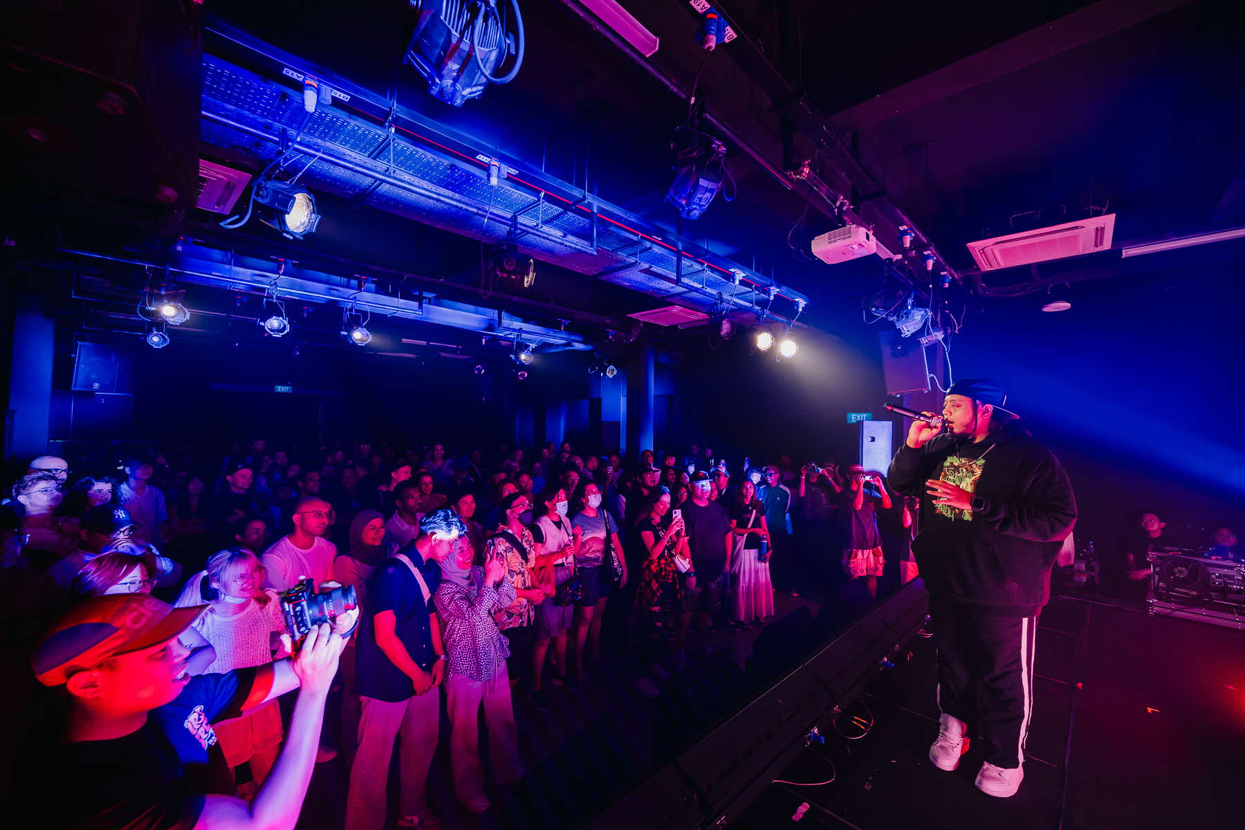 Image of a singer/rapper performing to a crowd illuminated by purple and blue lights