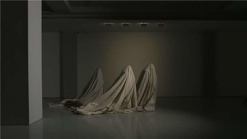 Image of a dark studio with long beige cloth covering an eerie looking structure