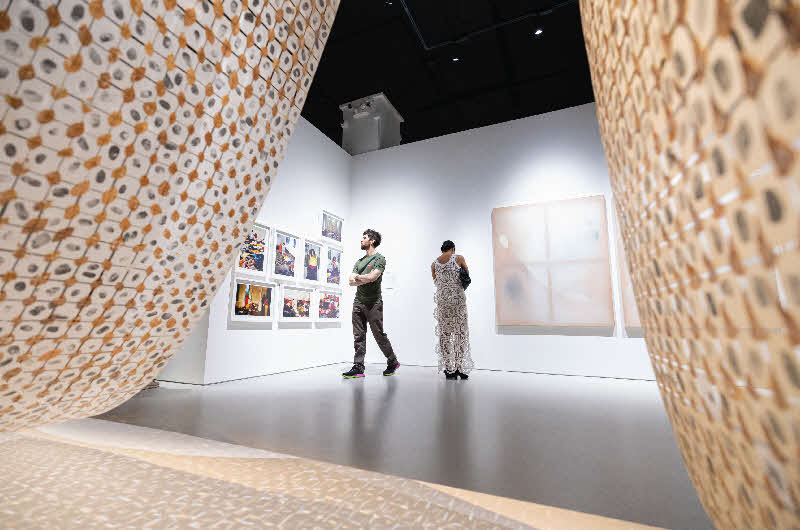 Photo of two installation artworks in foreground in a gallery space, with two people looking at the artwork on the walls in the background