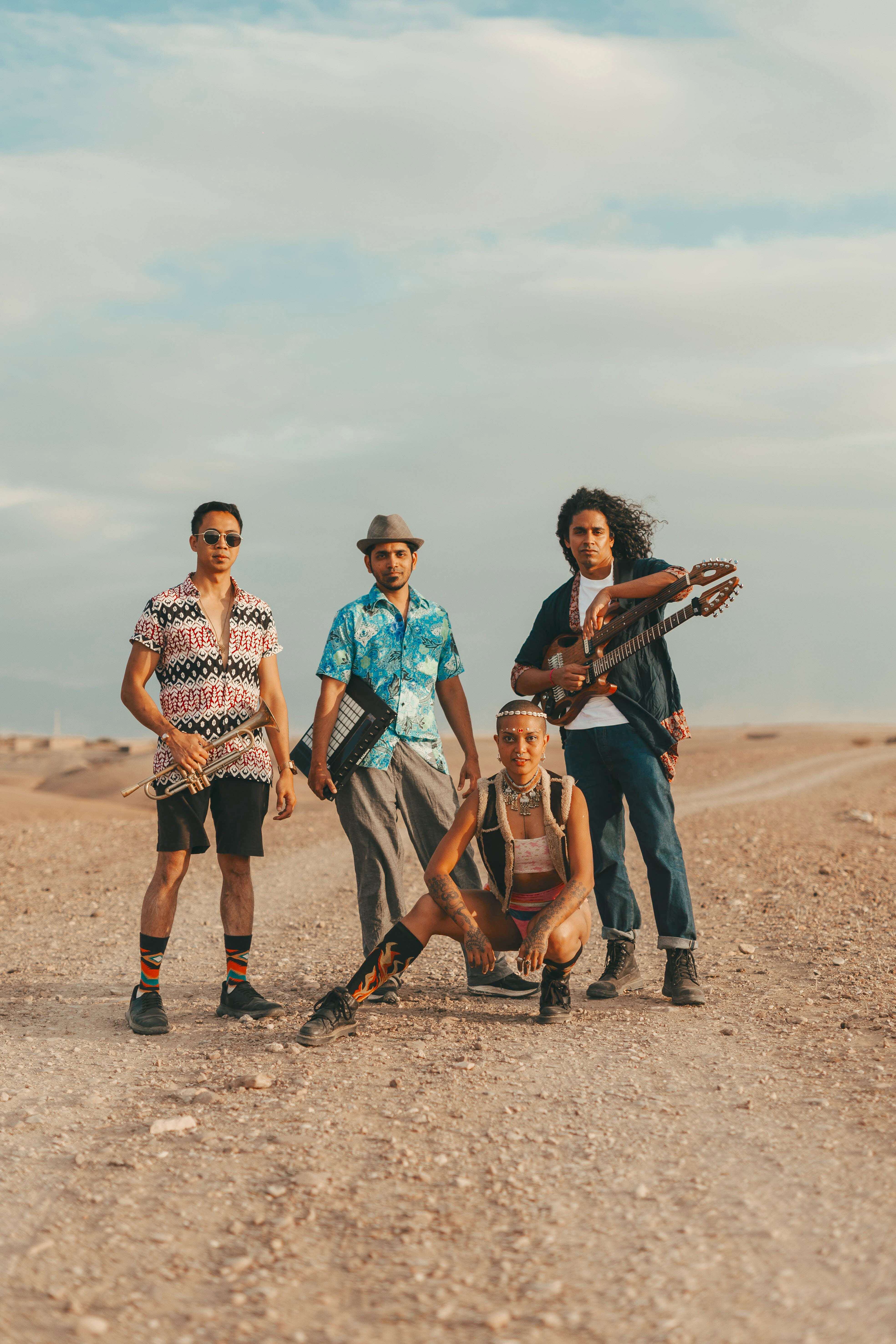 3 men and a woman standing on the sand looking into the camera