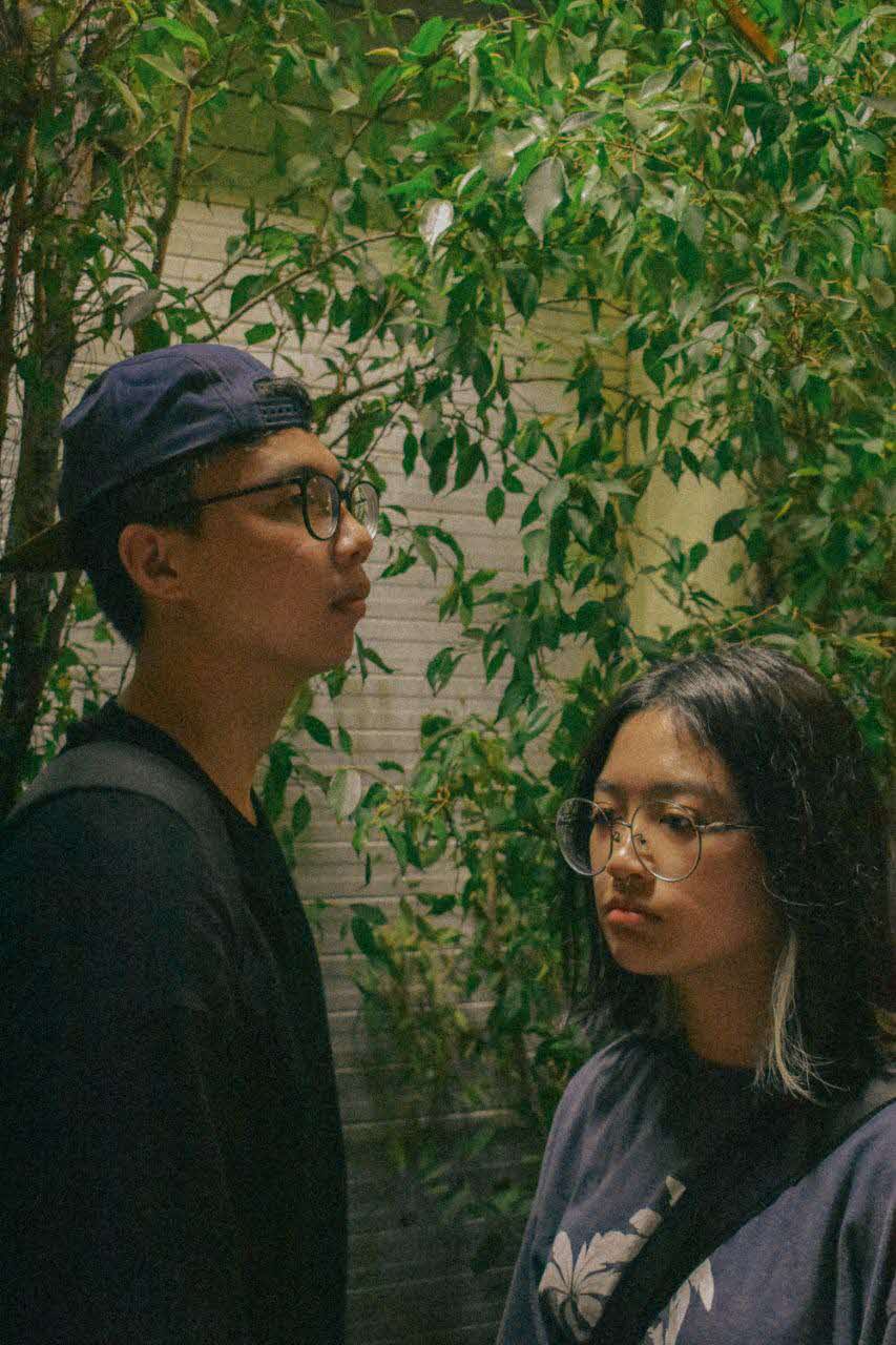 Young man and young woman standing under a tree in front of shutters